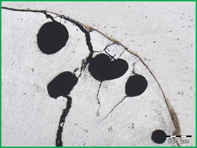 Obraz z mikroskopu optycznego przedstawiający pęcherze w złączu spawanym i propagujące od nich pęknięcia