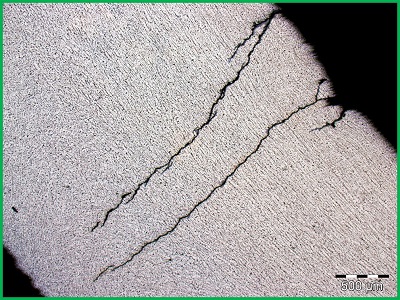 Obraz z mikroskopu optycznego przedstawiający poprzeczne pęknięcia naprężeniowe zainicjowane na wżerach korozyjnych